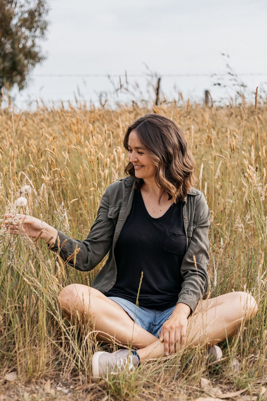 Amanda examining dandelion while sitting in field of grass.